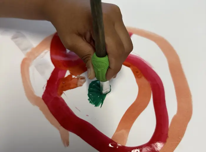 Grafomotorik: Eine Hand hält einen Pinsel mit Haltehilfe und malt bunte Kringel auf Papier.