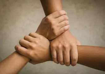 Drei Hände, die sich im Dreieck an den Handgelenken fassen.